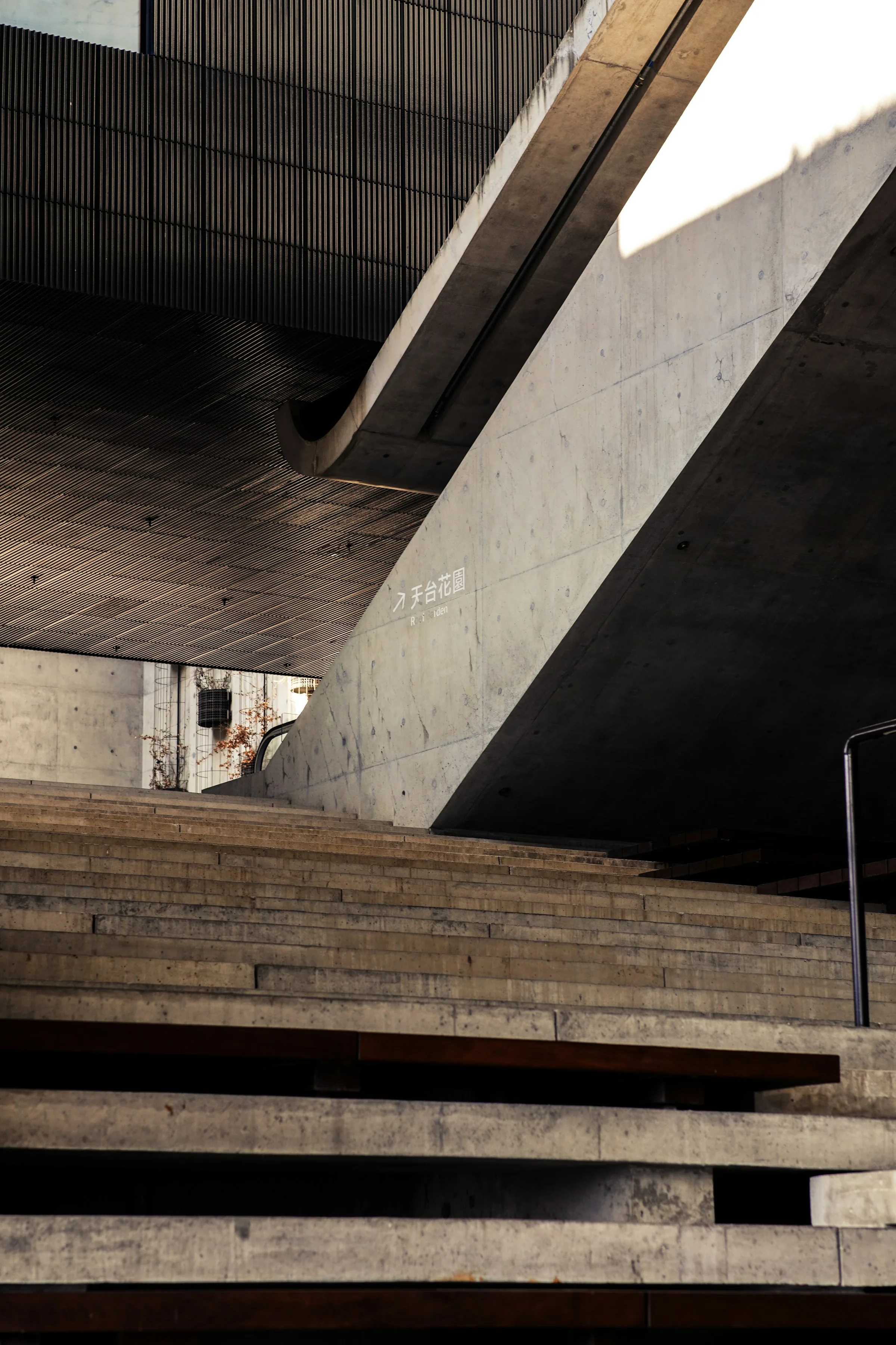 Concrete stair flights crossing at angles, cut by hard diagonal shadow